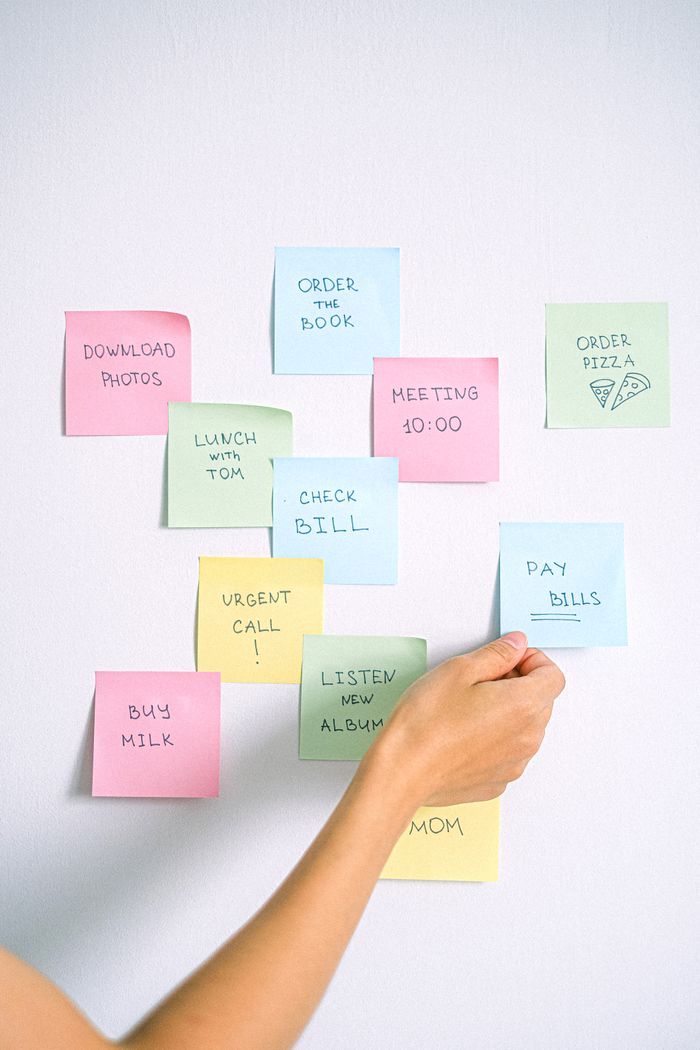 Contact A hand arranging colorful sticky notes with tasks on a white wall.