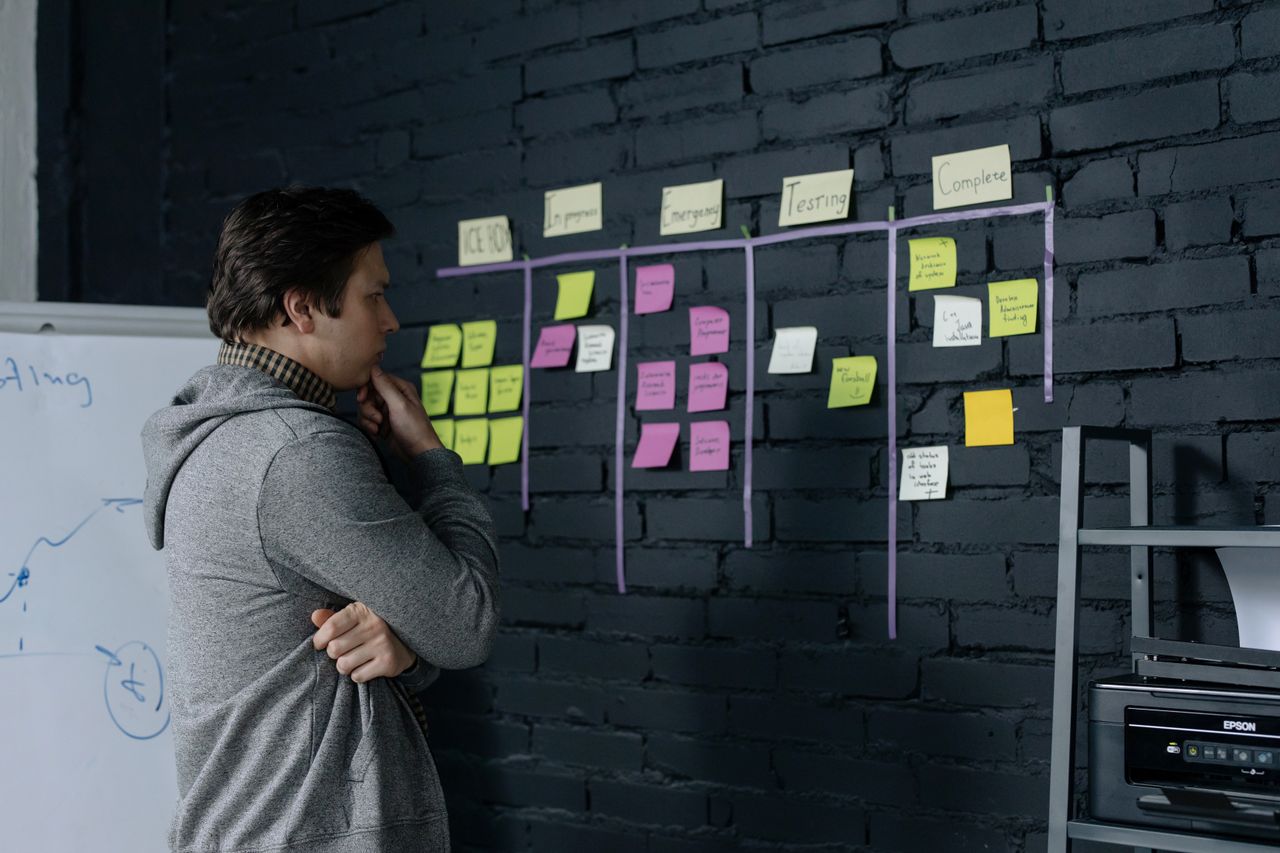 About Adult male focusing on task planning using sticky notes on a black wall in a contemporary office setting.